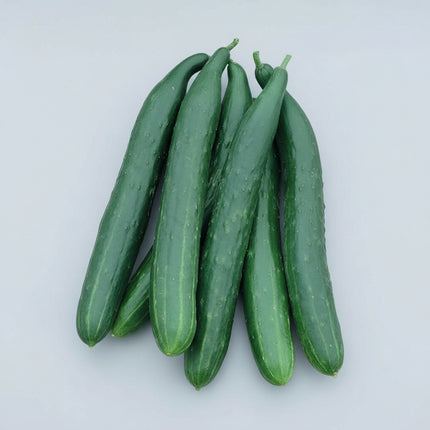 Several long, dark green cucumbers resting in a woven basket among green leaves and small yellow flowers.
