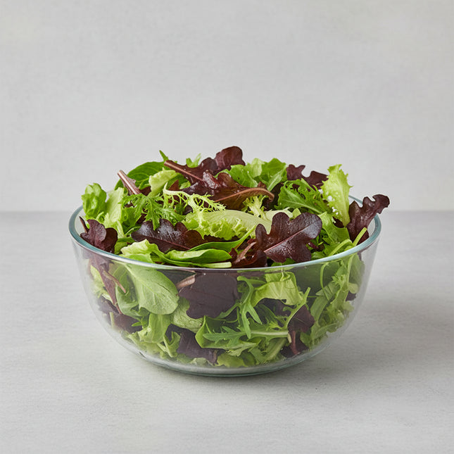 A close-up of mixed leaf lettuce growing in a garden bed, showing both green and burgundy-red varieties with speckled leaves. A Savvy Gardening logo watermark is visible in the bottom right corner.